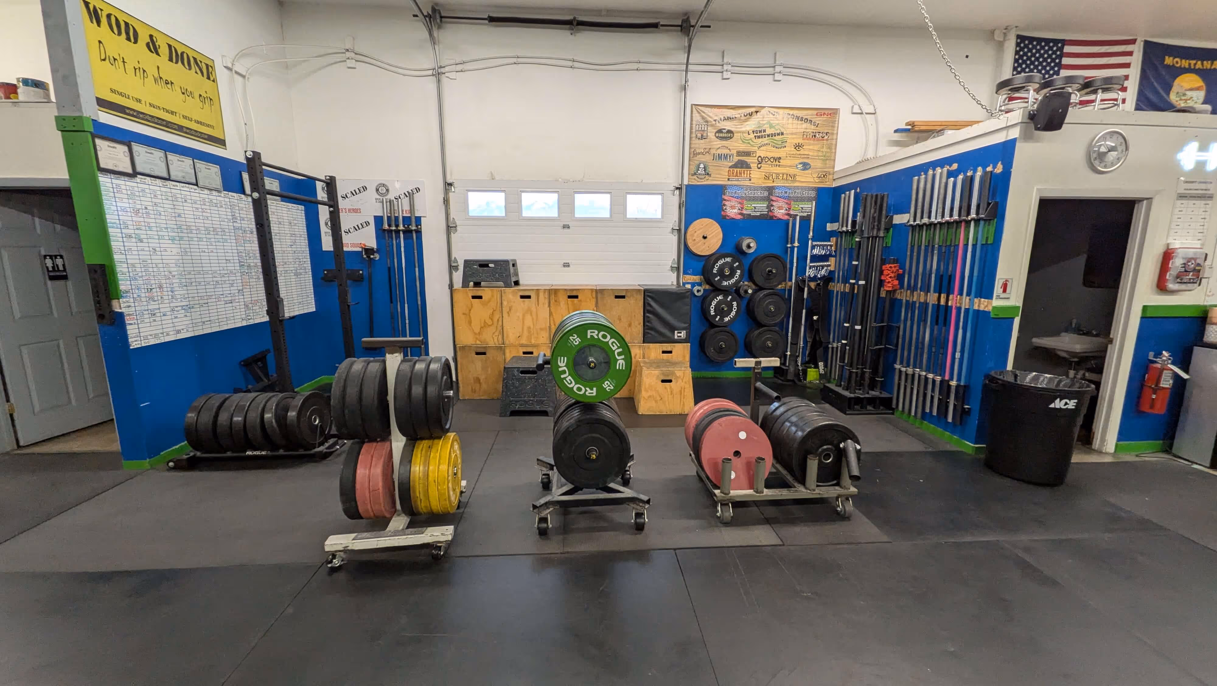 Interior of a CrossFit gym with weight plates, barbells, wooden boxes, and fitness equipment neatly arranged. Trailhead Physical Therapy and Performance