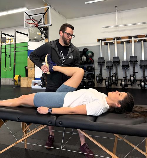 Physical therapist assisting woman lying on a massage table with bent knee stretch in a gym setting. trailhead-physical-therapy