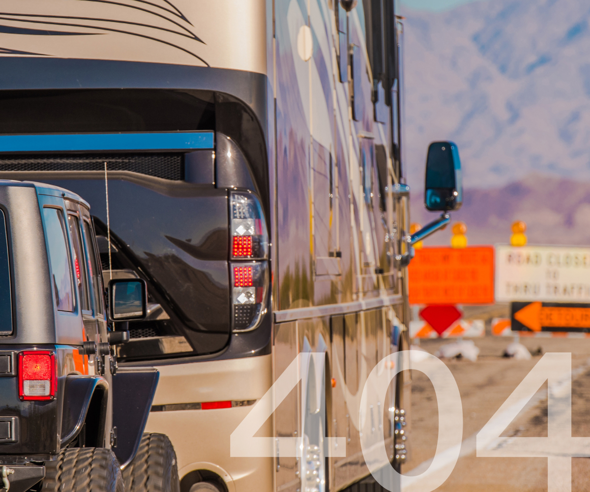 Close-up of a black jeep and a large RV with mountain background and road closure signs.