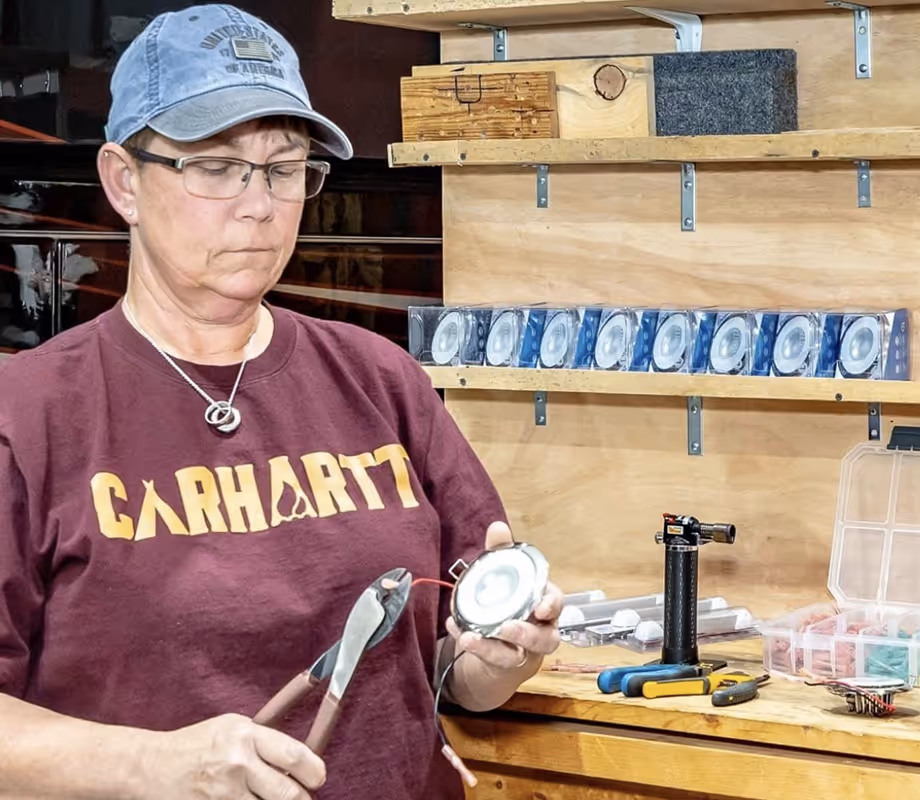 Person wearing a Carhartt shirt and cap working with wiring and tools in Hawkins Pointe's workshop.