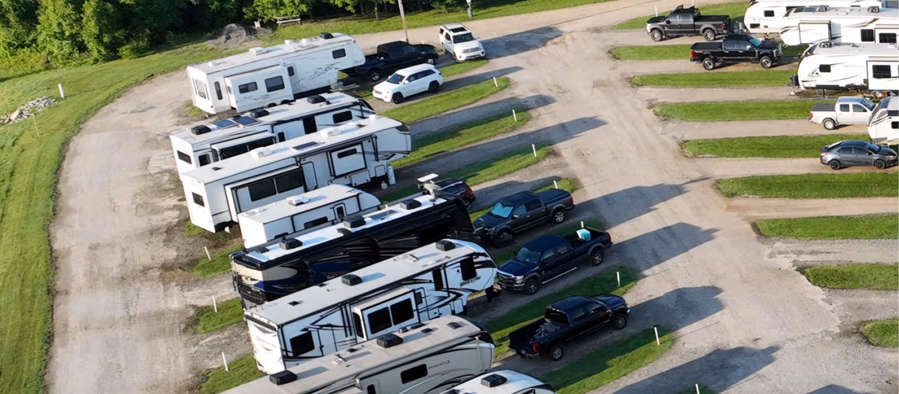Aerial view of an Hawkins Pointe RV park with multiple recreational vehicles and trucks parked beside gravel lanes surrounded by green grass.