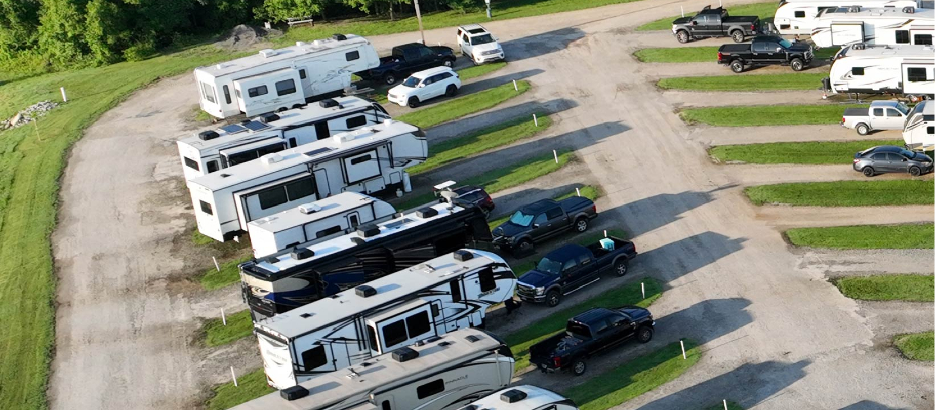 Aerial view of an Hawkins Pointe RV park with multiple recreational vehicles and trucks parked beside gravel lanes surrounded by green grass.