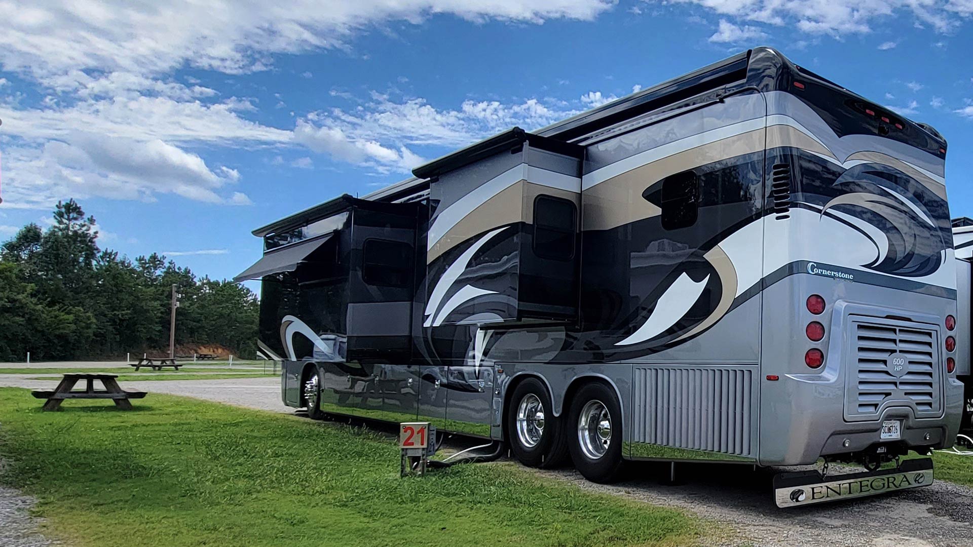 Large black and silver luxury motorhome with slide-outs parked at RV site #21.