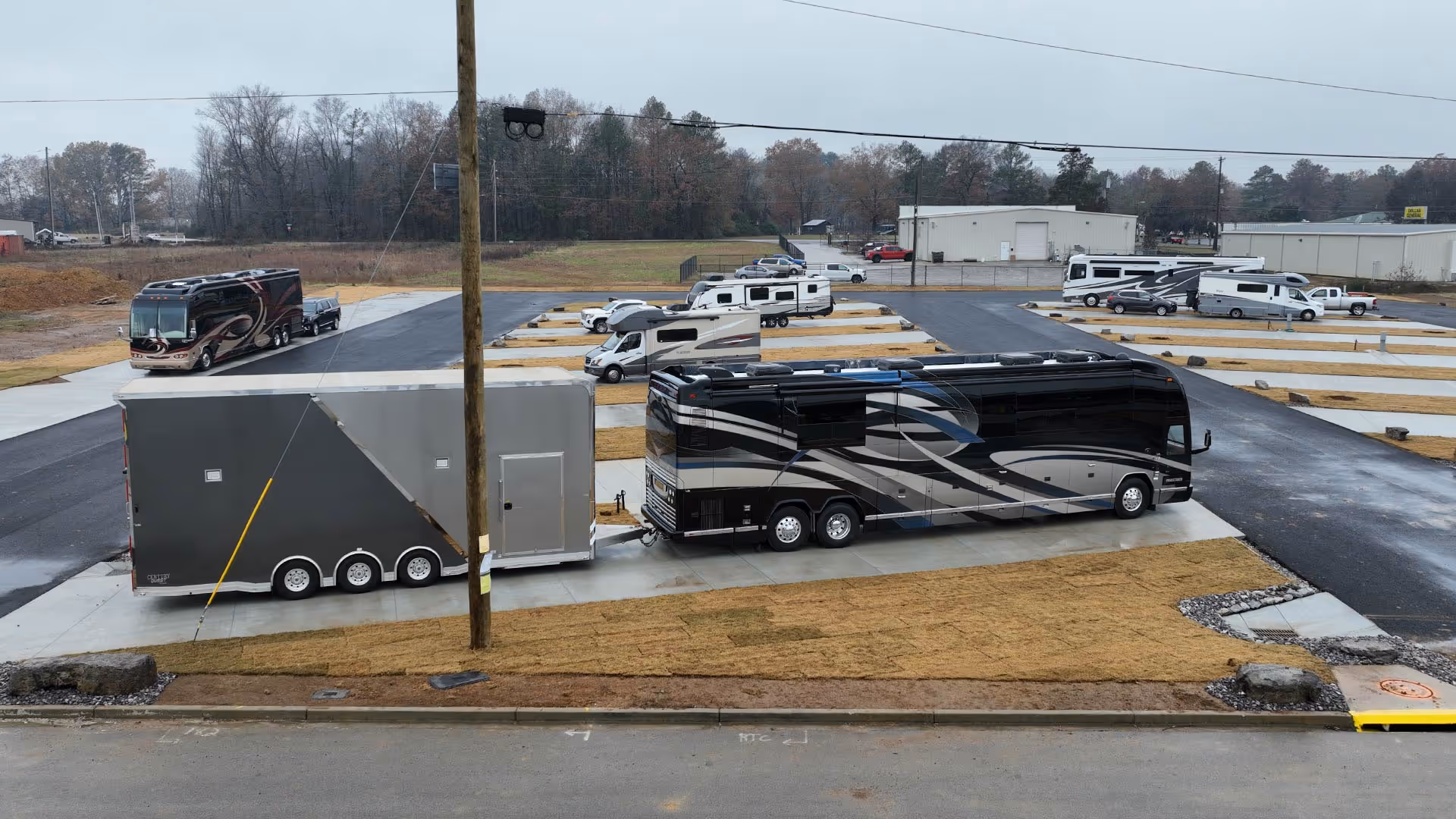 Black and gray luxury motorhome with attached trailer parked on a concrete pad.