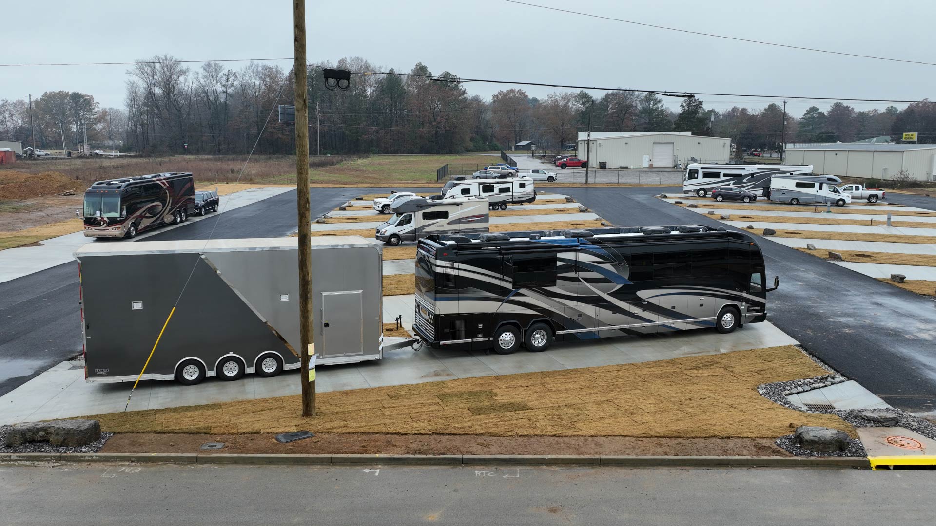 Black and gray luxury motorhome with attached trailer parked on a concrete pad.