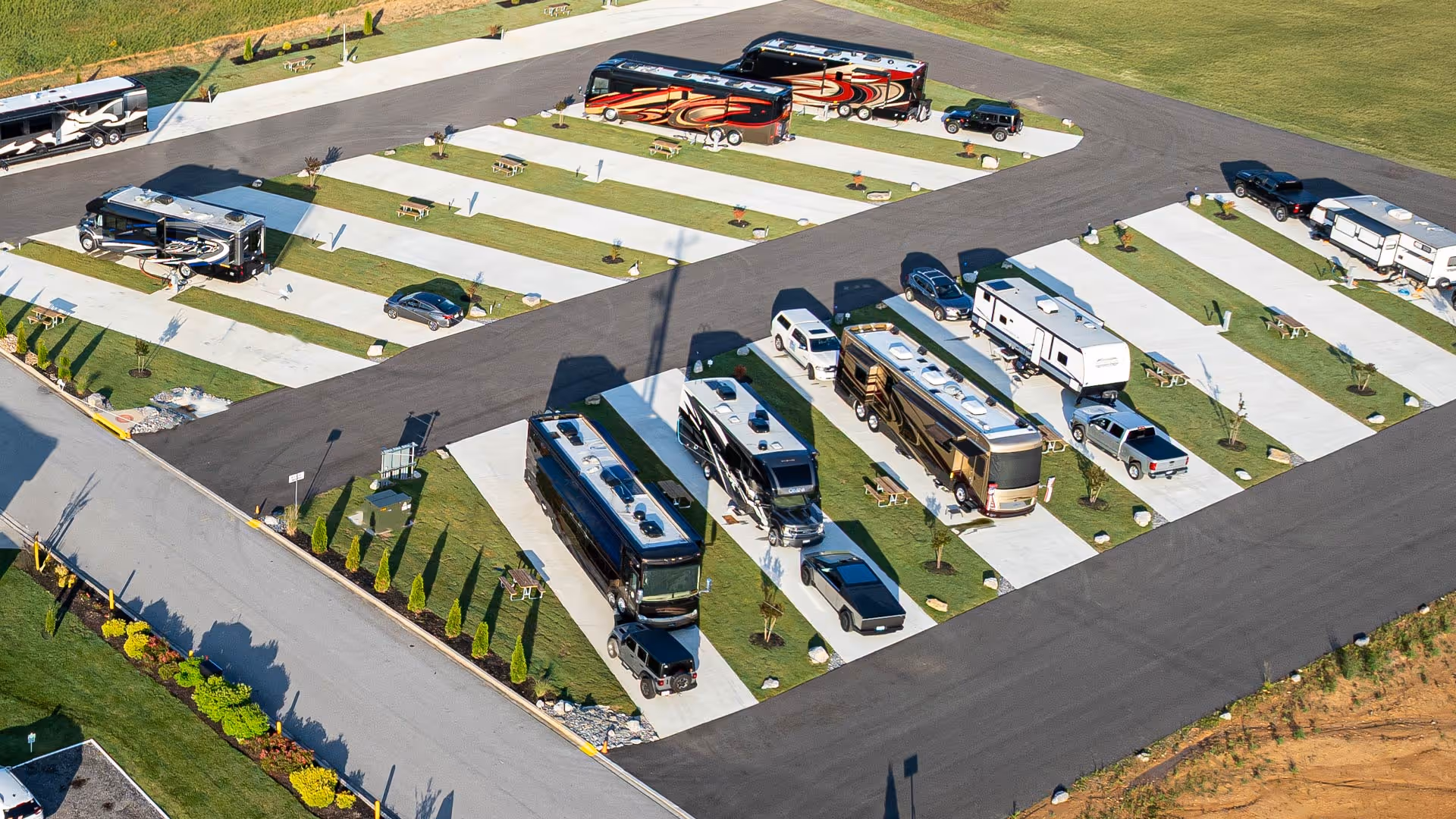 Aerial view of Executive RV sites with multiple parked recreational vehicles, trucks, concrete pads, picnic tables, and green grassy areas.