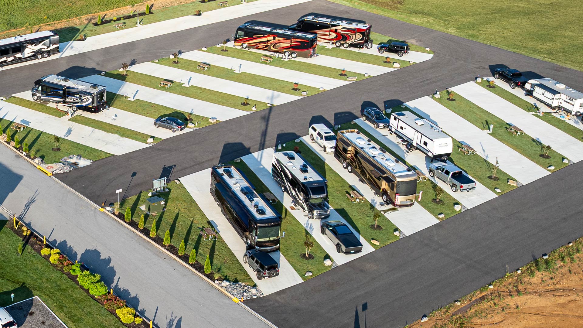 Aerial view of Executive RV sites with multiple parked recreational vehicles, trucks, concrete pads, picnic tables, and green grassy areas.