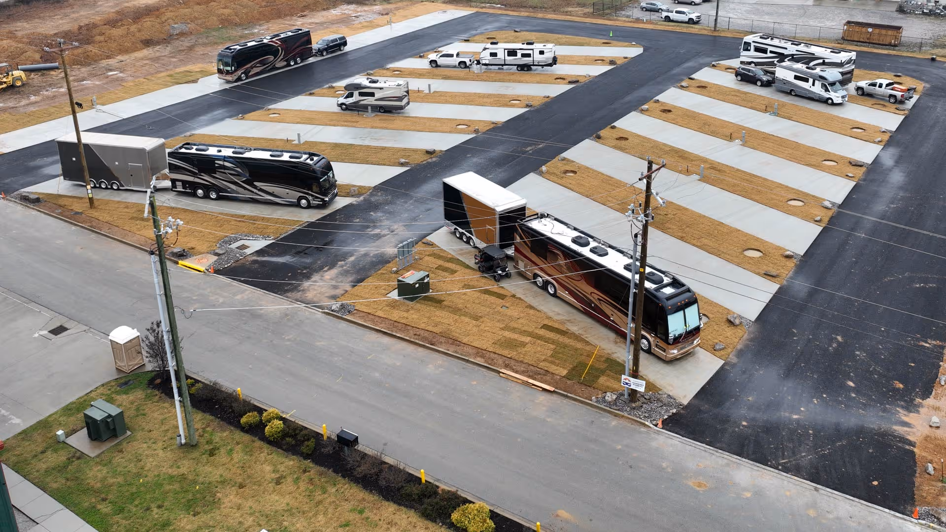 Aerial view of an RV park with multiple motorhomes and trailers parked on concrete pads separated by grassy areas.