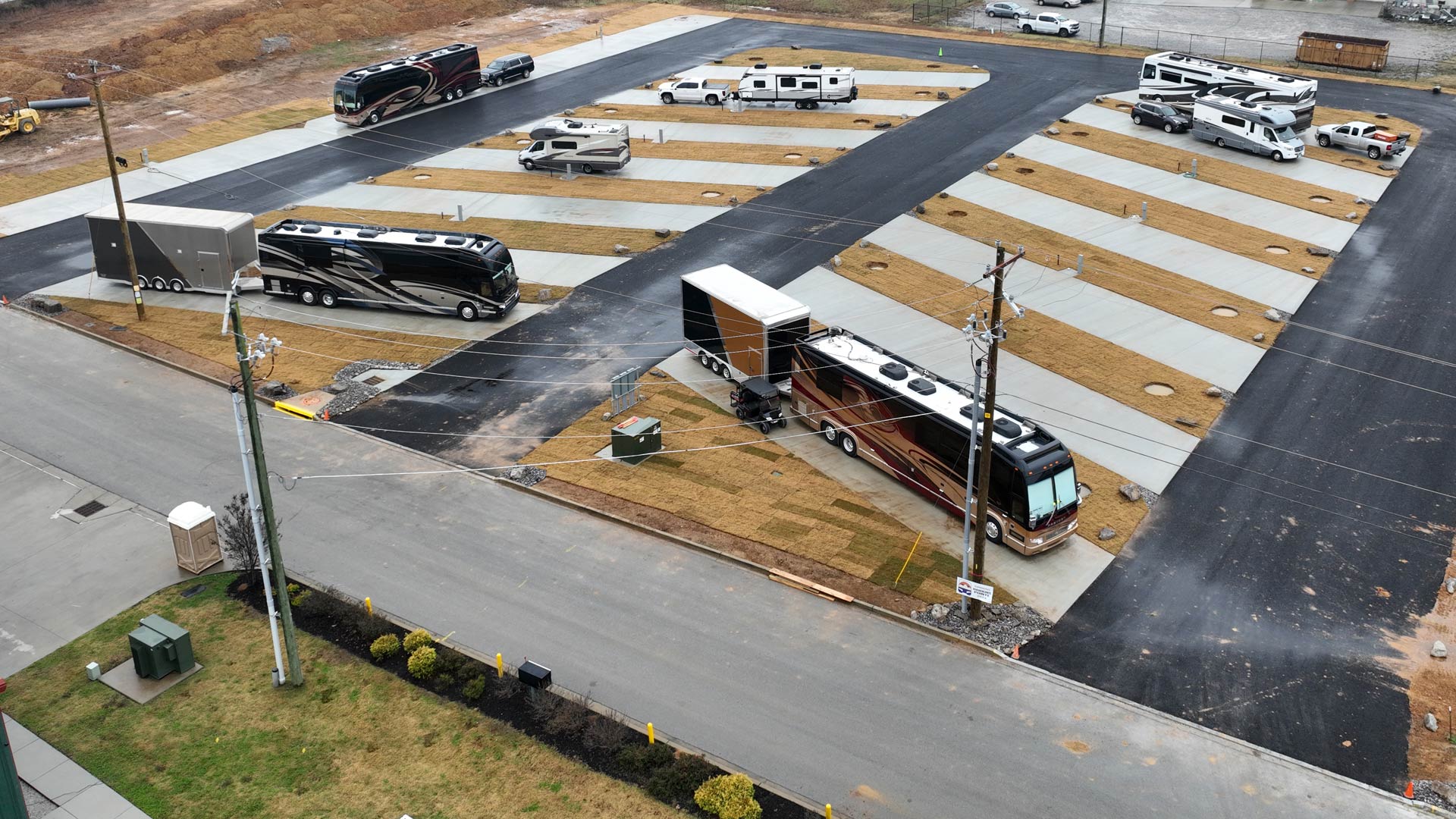 Aerial view of an RV park with multiple motorhomes and trailers parked on concrete pads separated by grassy areas.