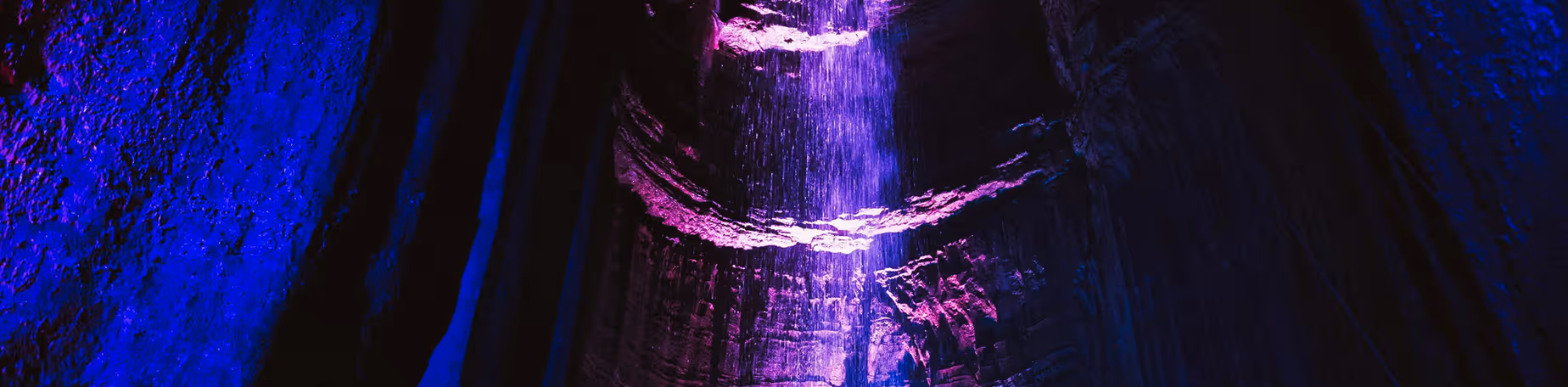 Ruby Falls illuminated with purple and blue lights flowing inside a dark cave.