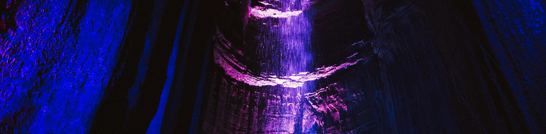 Ruby Falls illuminated with purple and blue lights flowing inside a dark cave.