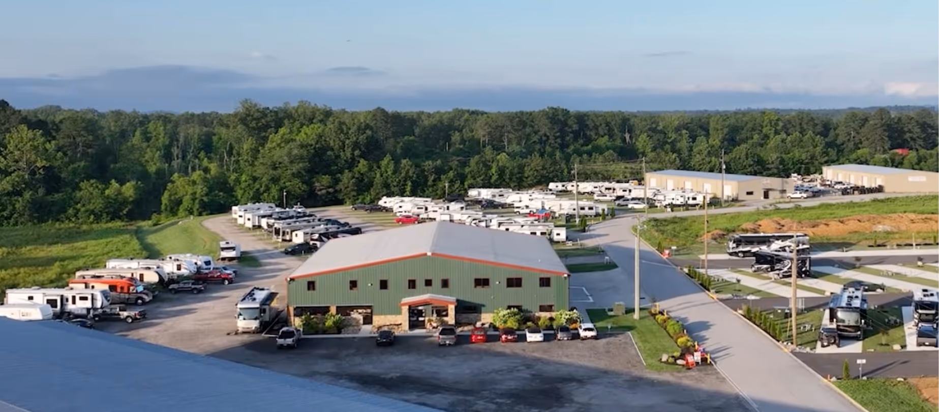 Aerial view of an Hawkins Pointe RV park with multiple parked recreational vehicles and a large green building surrounded by trees.