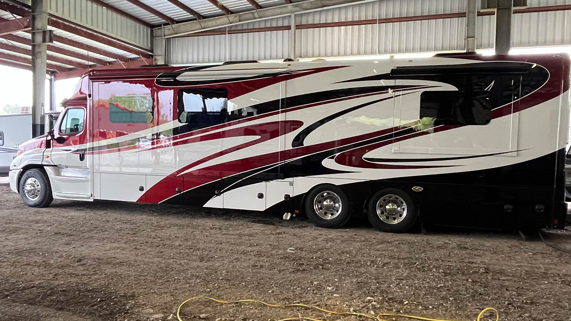 Large luxury motorhome with red, white, and black swirling design in our covered storage area.