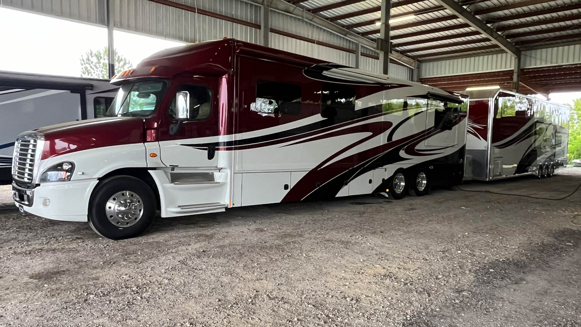 Large maroon and white RV with an attached matching trailer parked inside our covered storage area.