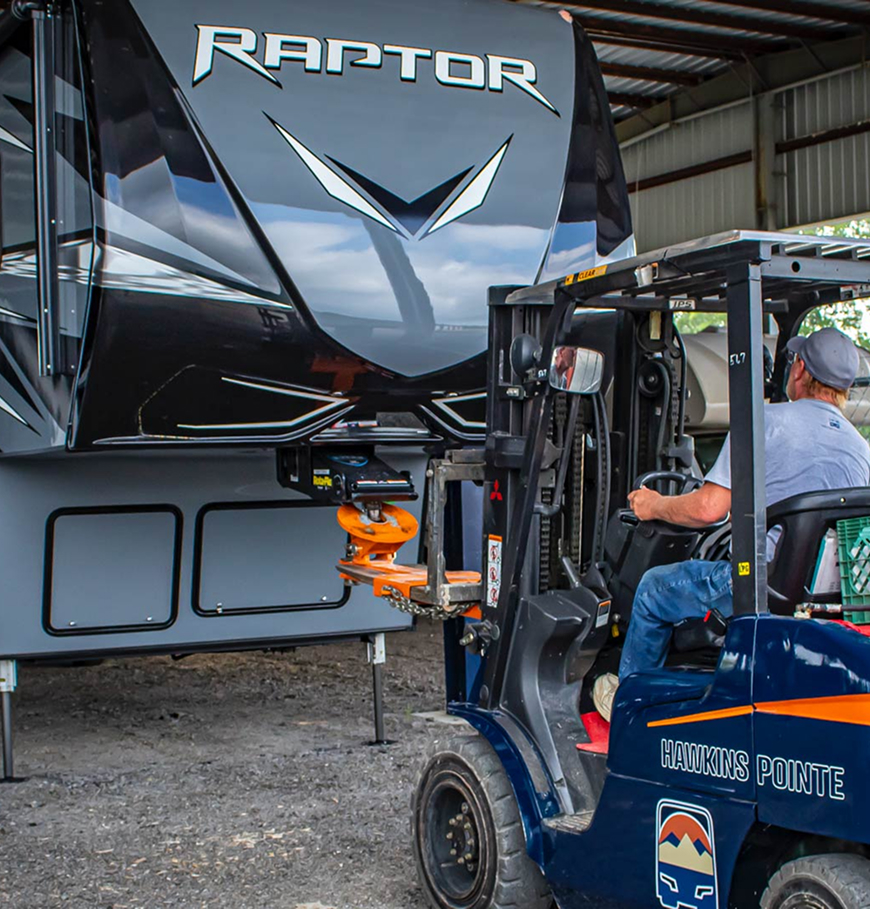 Staff operating a Hawkins Pointe forklift lifting a Raptor fifth wheel trailer hitch inside our covered storage facility. 