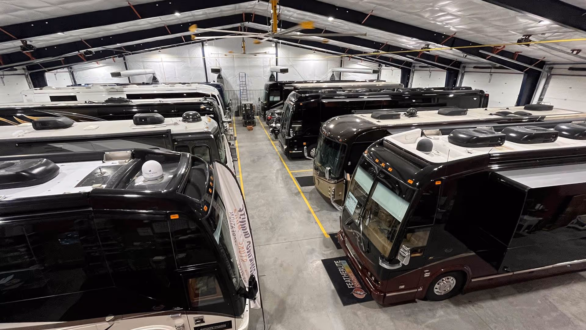Multiple luxury RVs parked inside our well-lit storage facility with a high ceiling and industrial fans.