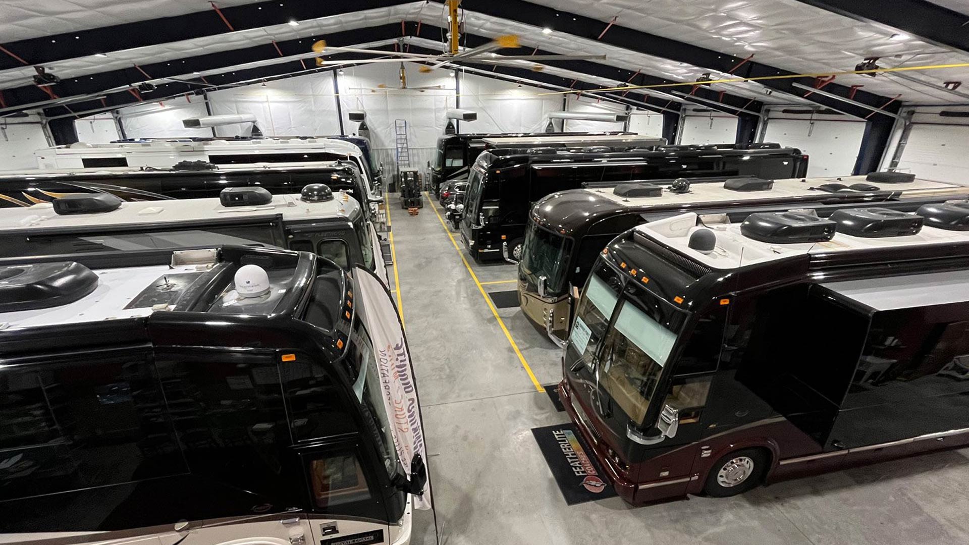 Multiple luxury RVs parked inside our well-lit storage facility with a high ceiling and industrial fans.