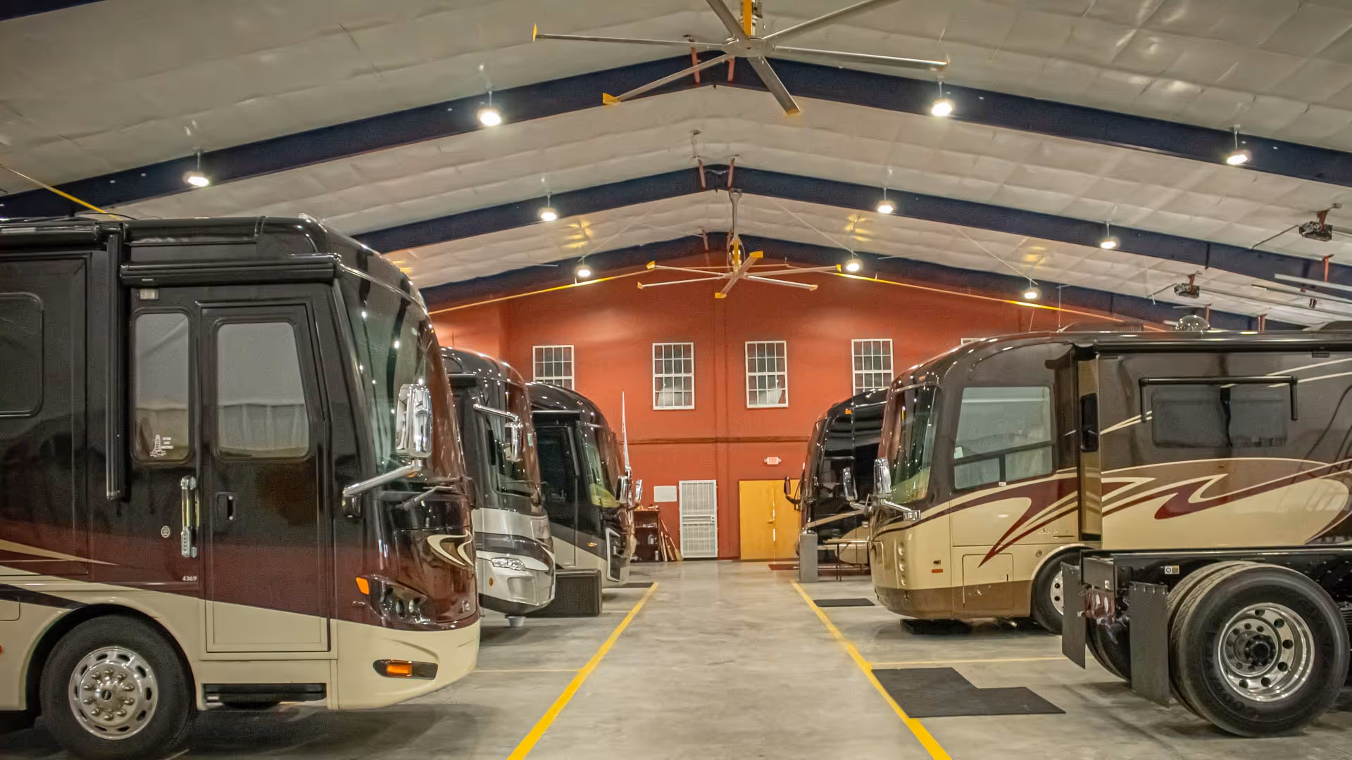 Luxury RVs parked on each side of our storage facility with high vaulted ceiling and industrial fans. 