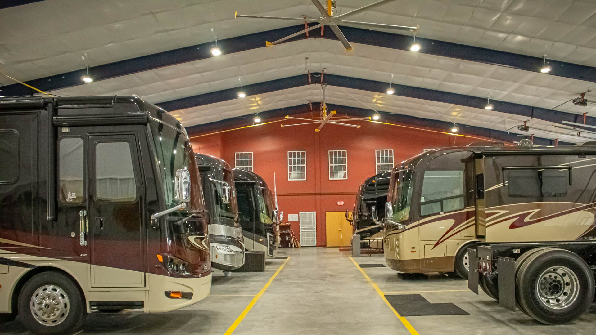 Luxury RVs parked on each side of our storage facility with high vaulted ceiling and industrial fans. 