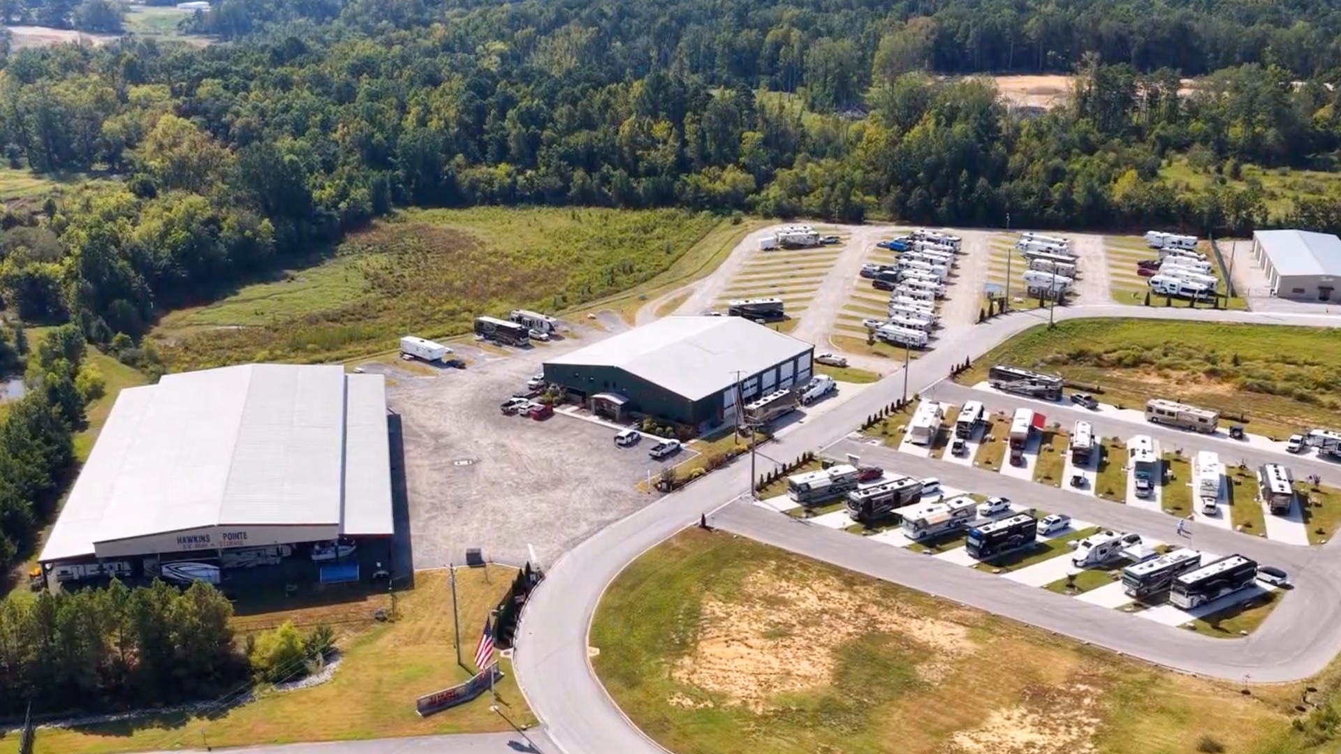 Aerial view of Hawkins Pointe RV Basecamp showing the main storage building, office, and rows of RVs parked along paved sites surrounded by trees.