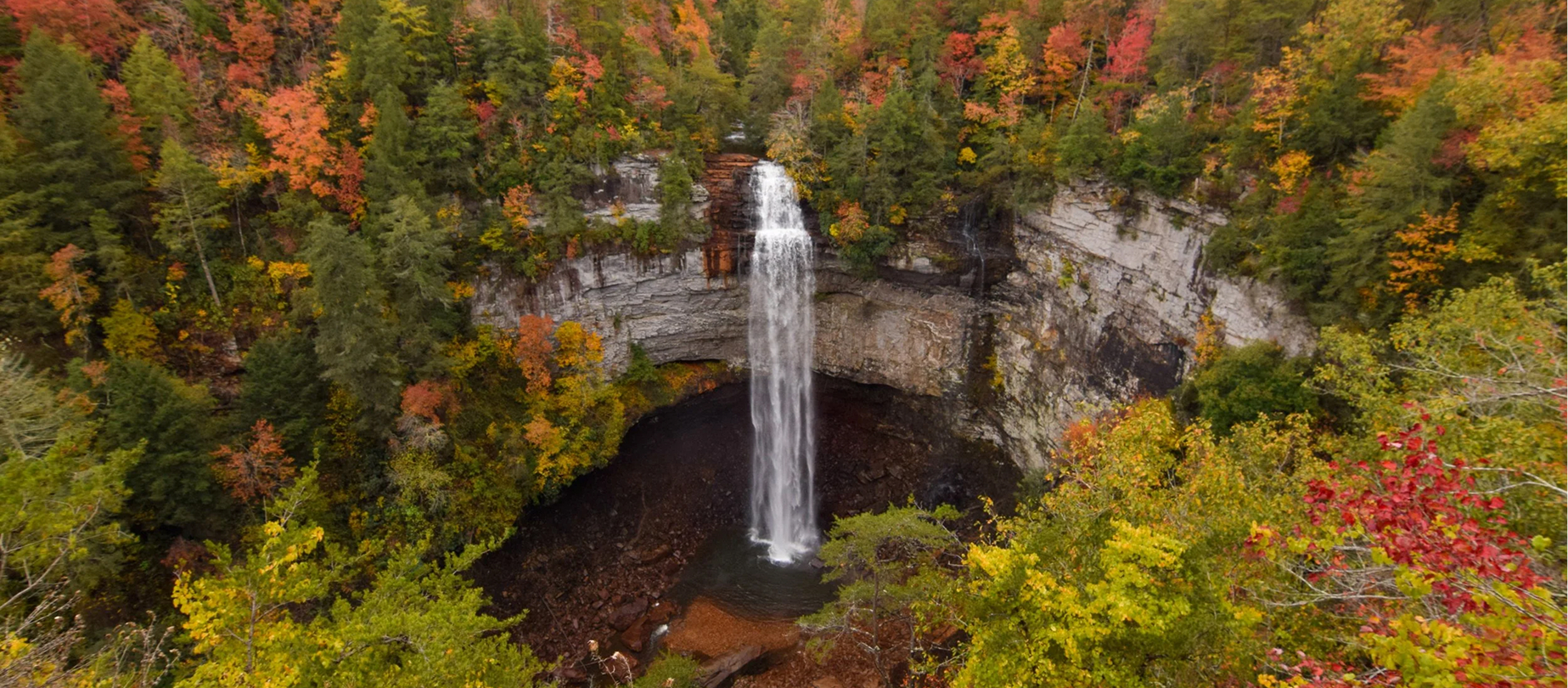 Waterfall plunging into a rocky gorge surrounded by red, orange, and gold fall foliage.