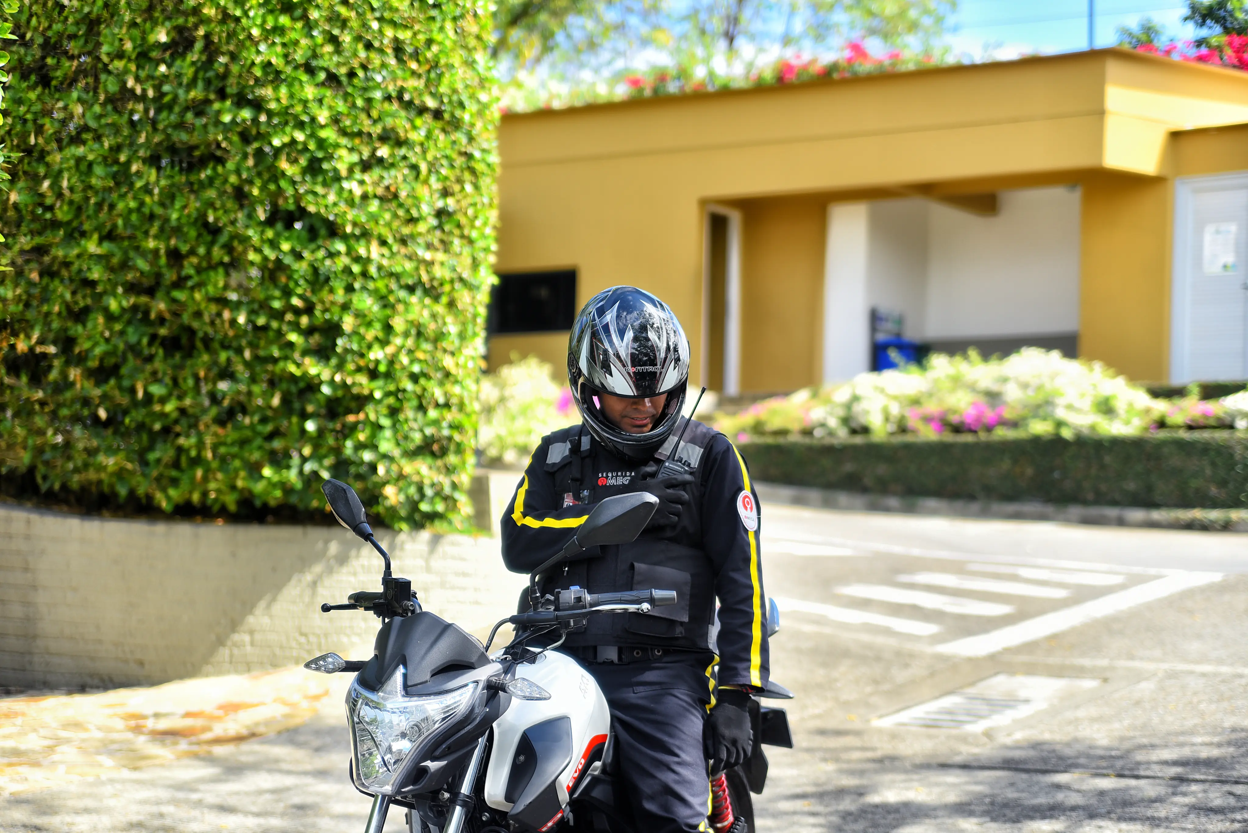 Motorcycle security guard in black helmet and uniform using a walkie-talkie while sitting on a white and black motorcycle.