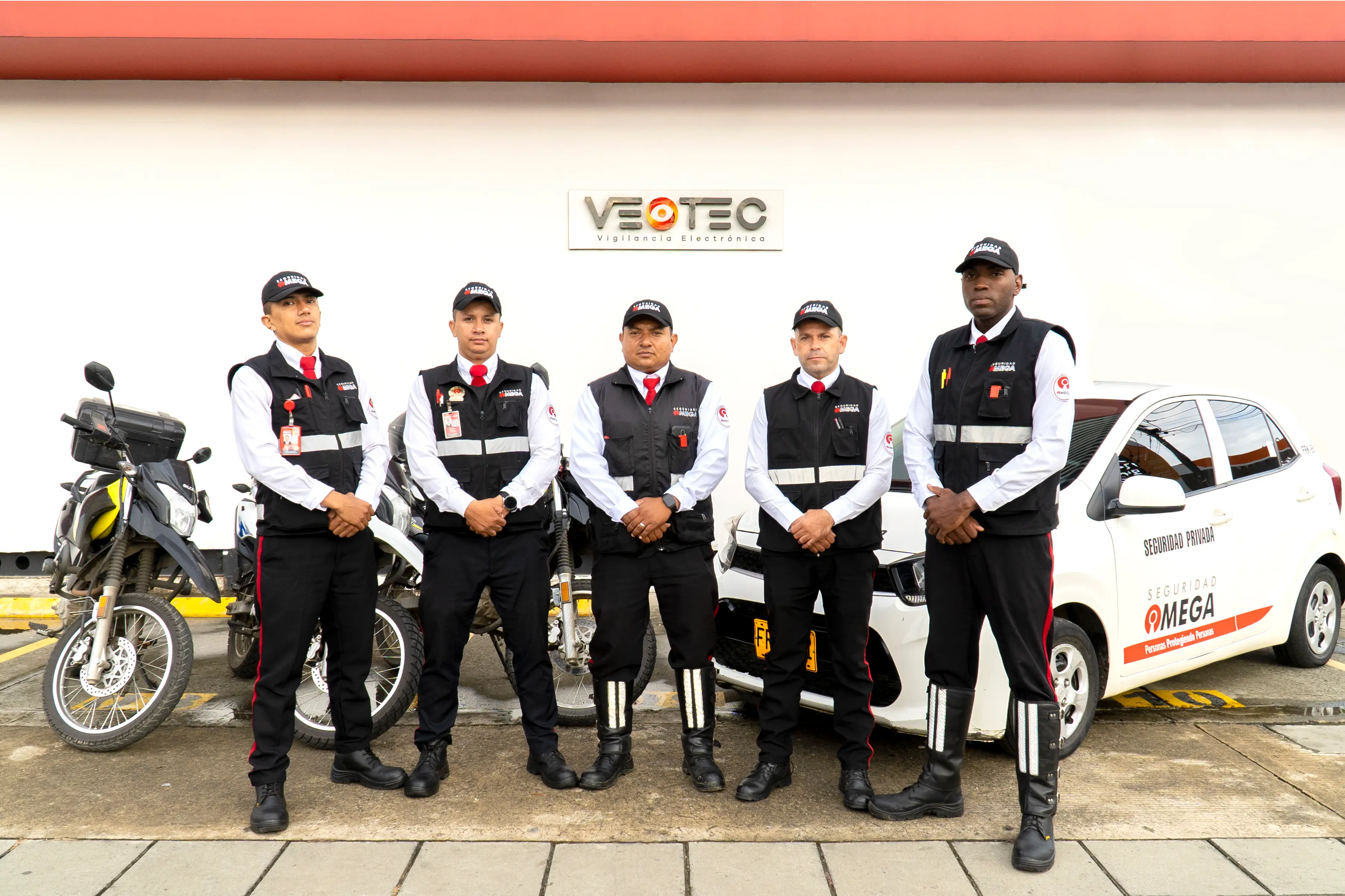 Five security guards in uniform standing in front of motorcycles and a white security car with 'Seguridad Omega' branding.