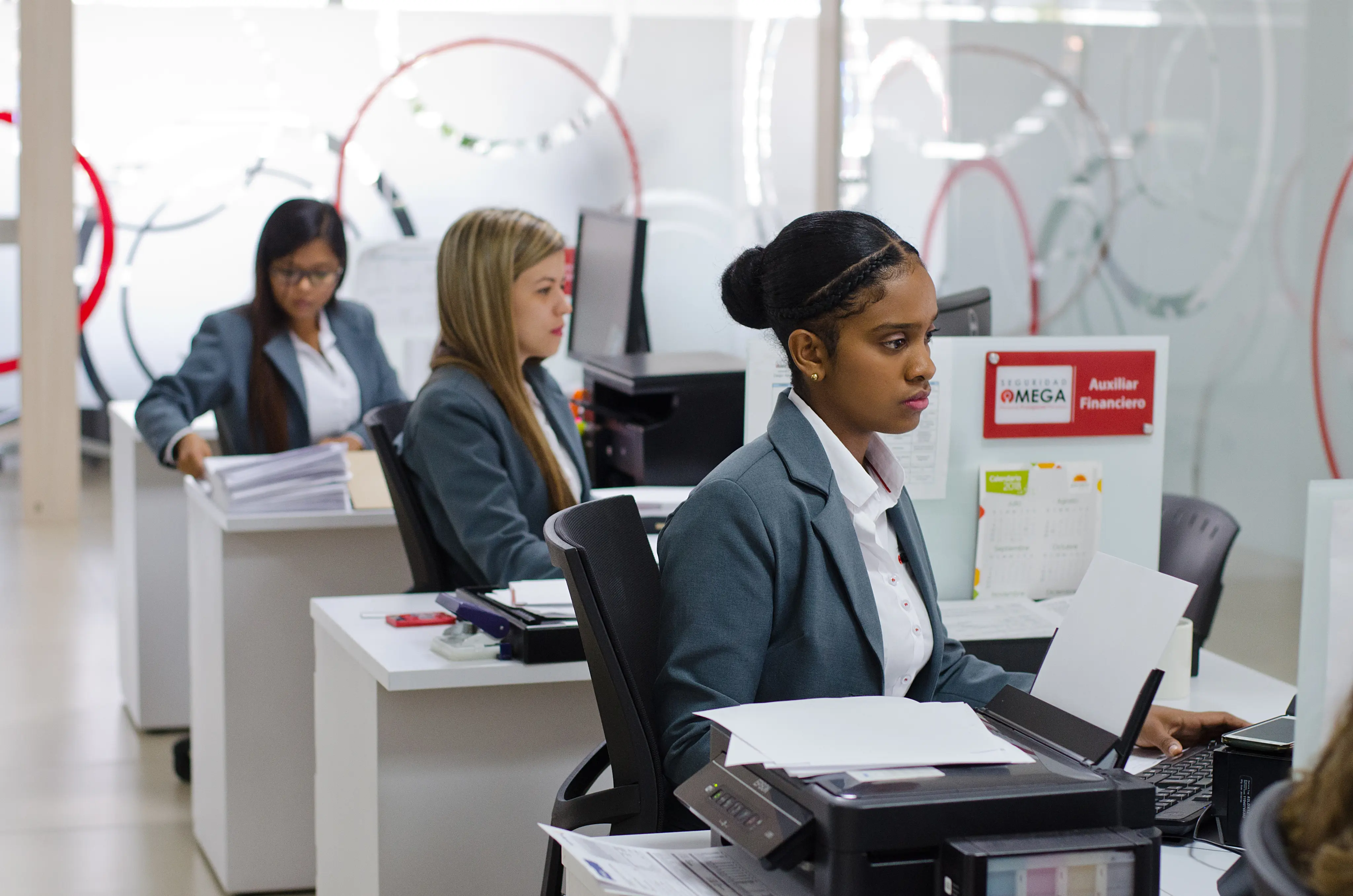 Three women in business attire working at individual desks in a modern office.