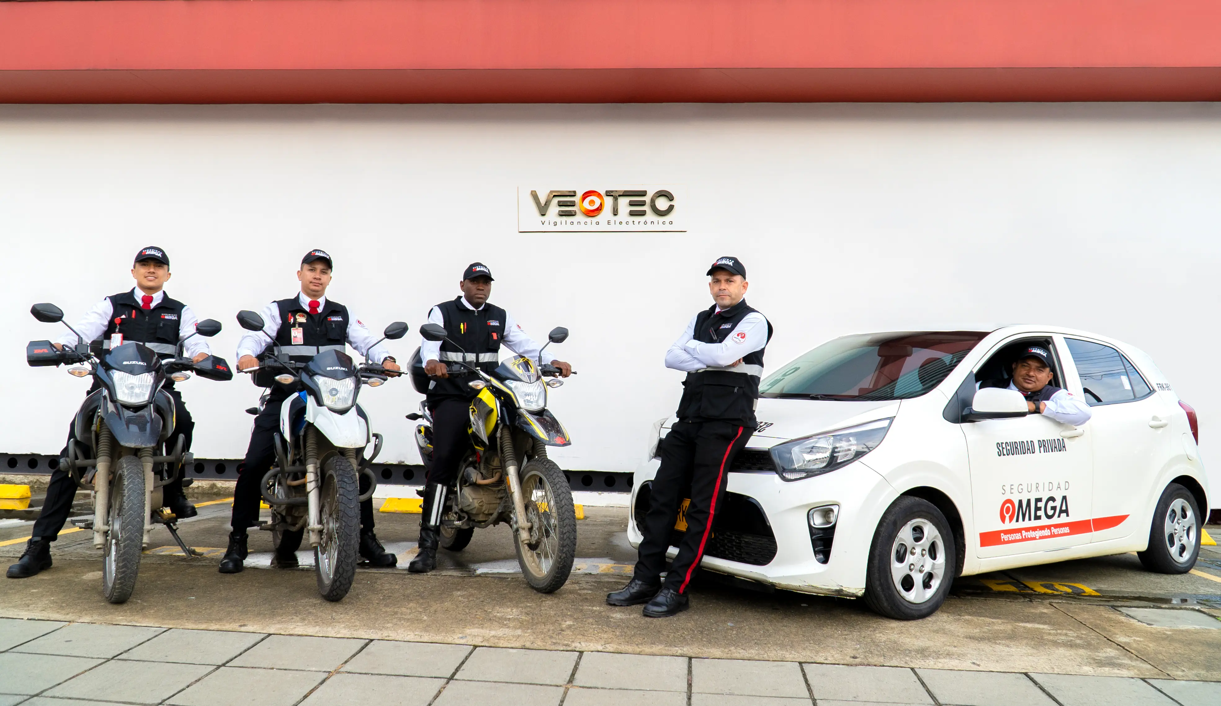 Four security guards in uniform with three motorcycles and one white car marked Seguridad Omega.