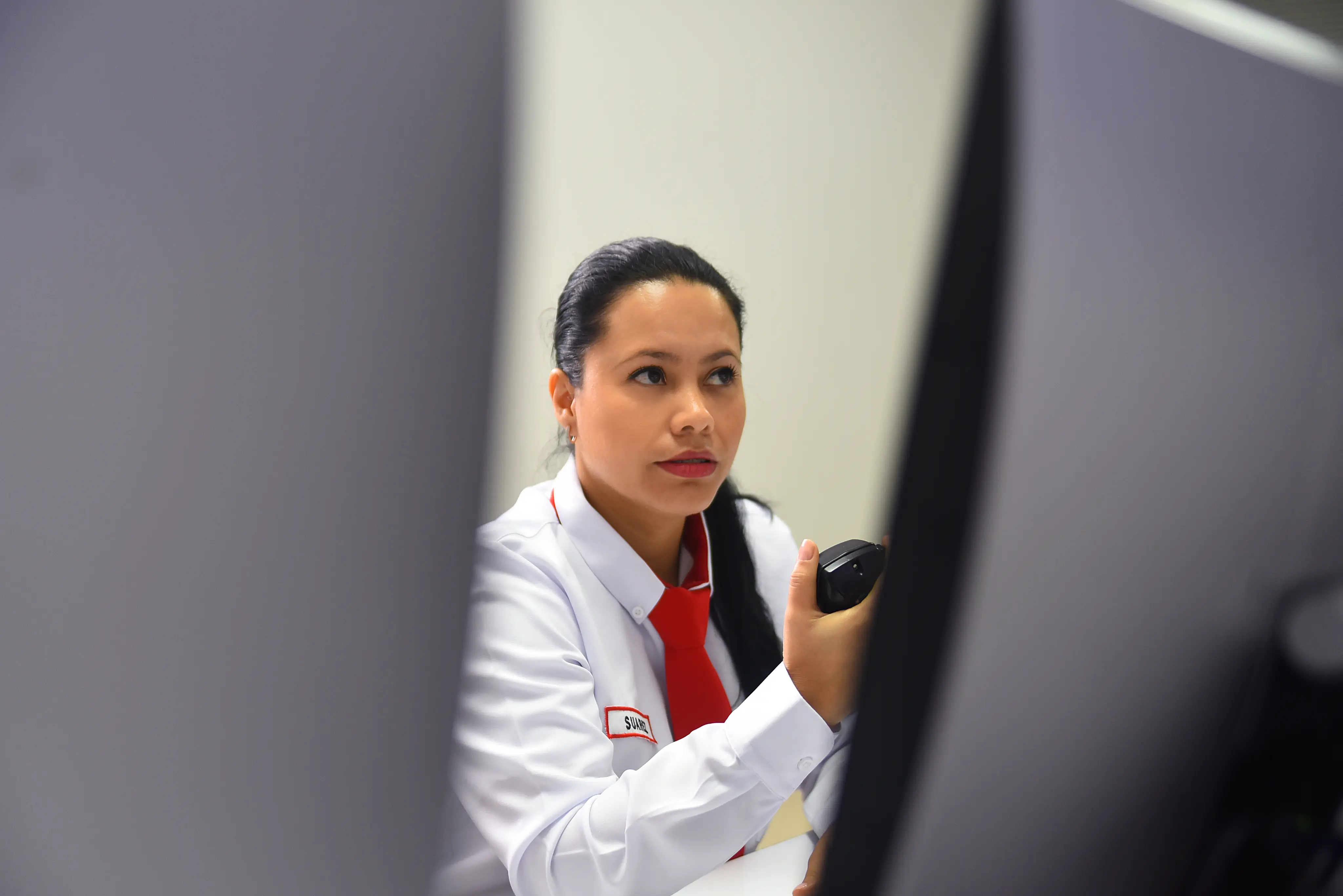 Female security guard in white uniform and red tie holding a walkie-talkie, looking attentively to the side.