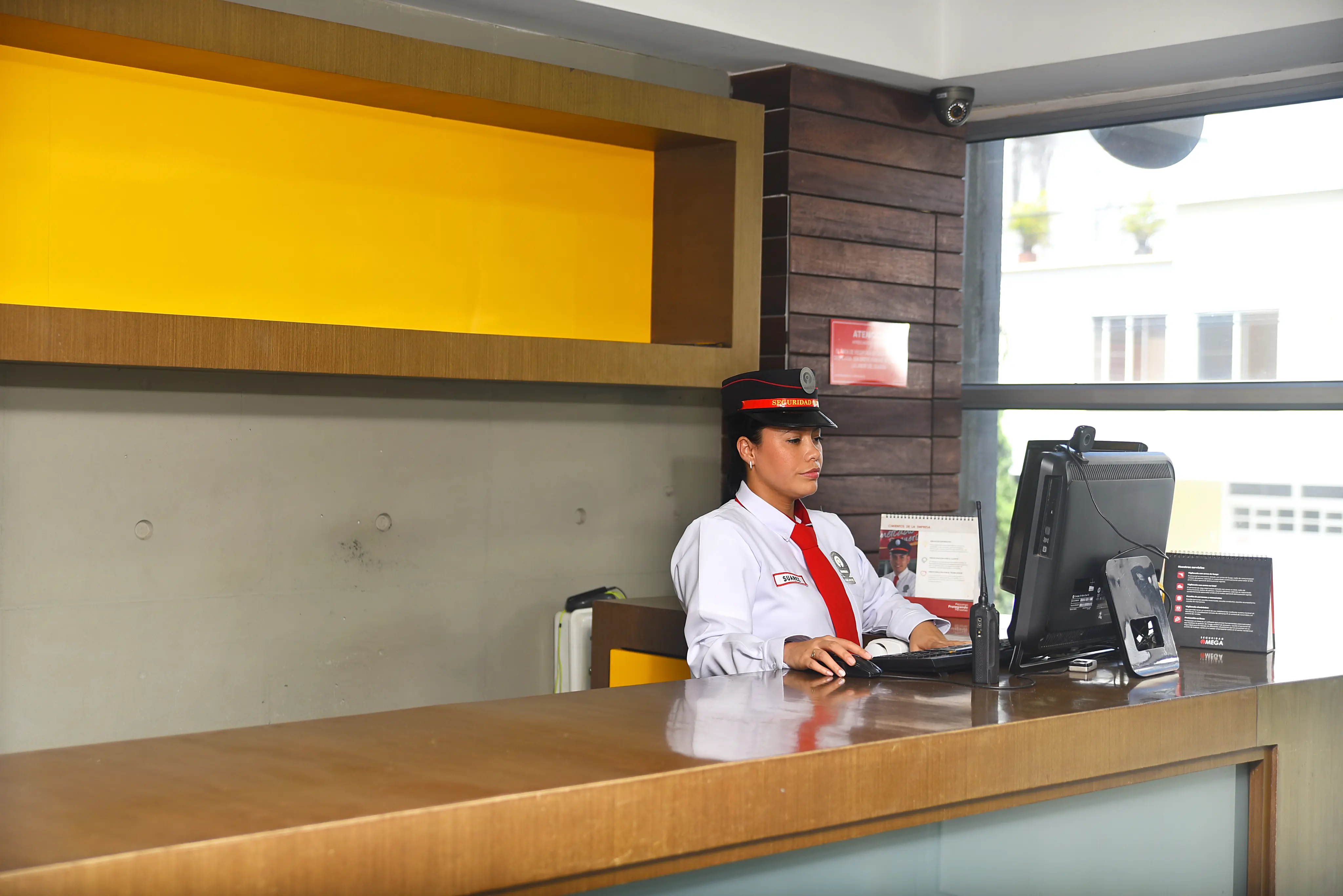 Security guard in uniform sitting at a reception desk working on a computer.