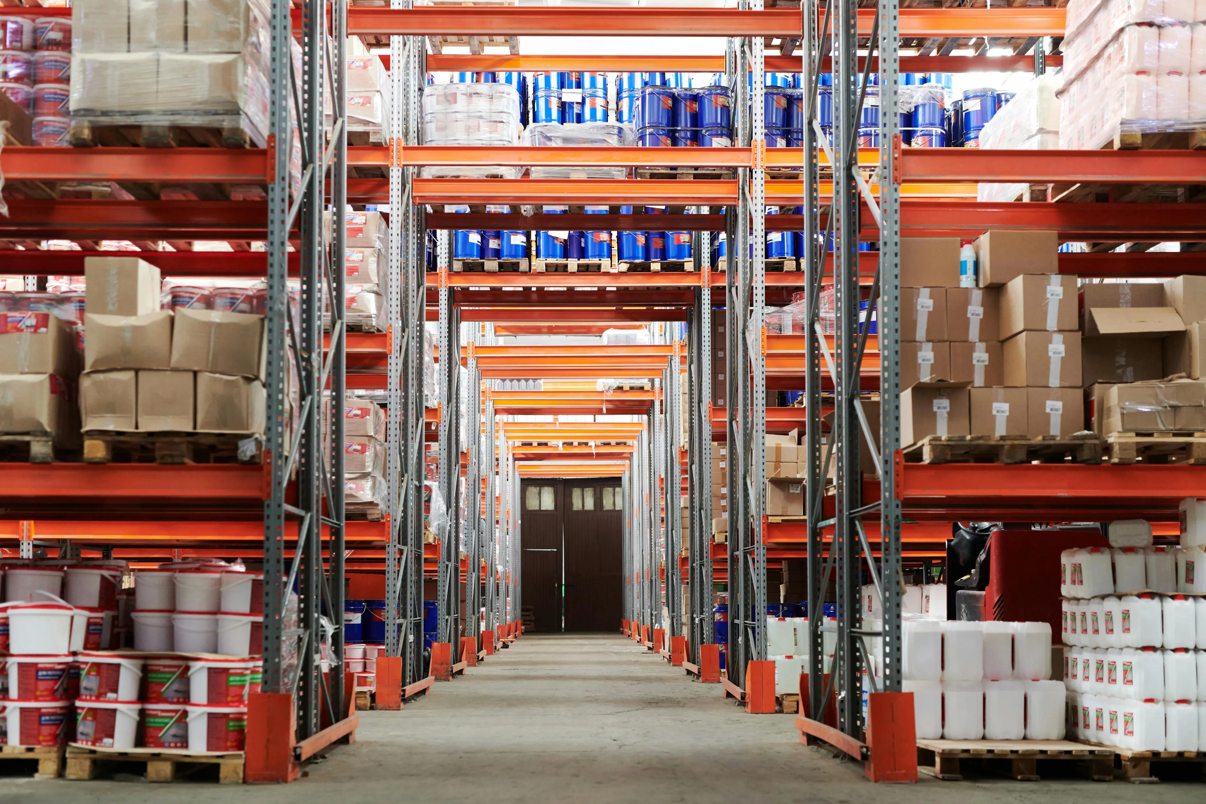 A warehouse aisle with tall metal shelves stocked with boxes, paint cans, and containers.