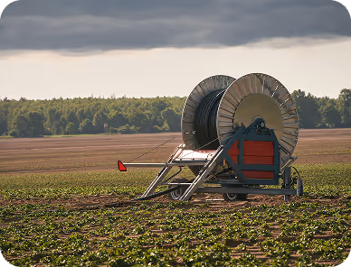 Irrigation reel machine on a green agricultural field under a cloudy sky.
