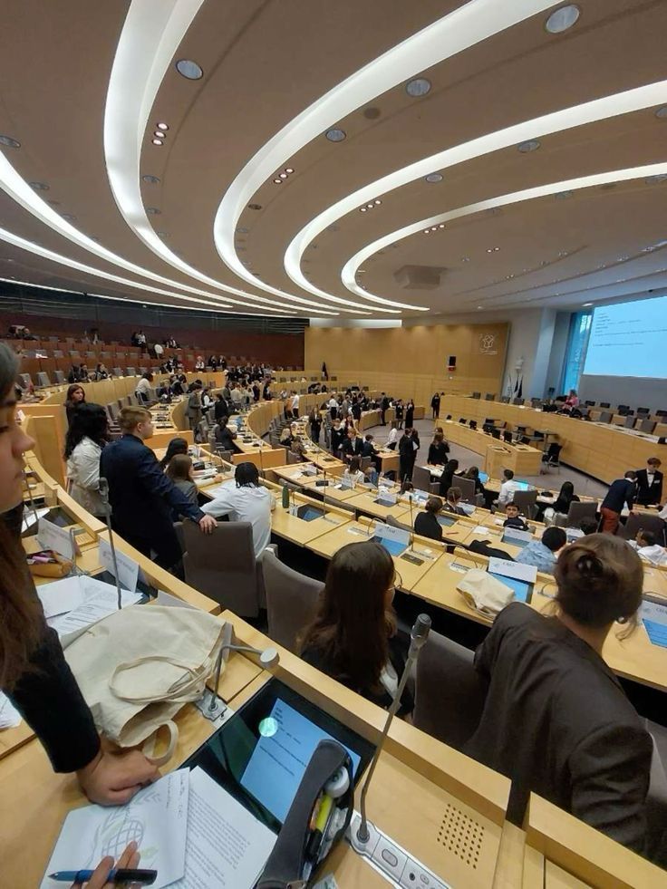Large conference room with curved seating, filled with numerous people attending a formal meeting or assembly.