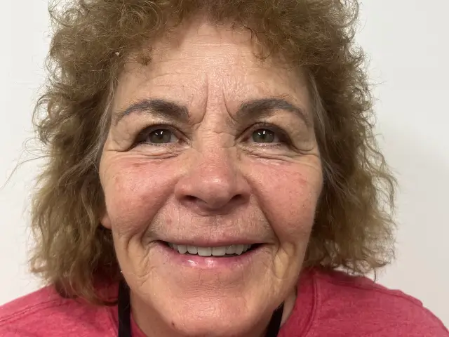 Smiling older woman with curly light brown hair wearing a red top against a plain white background.