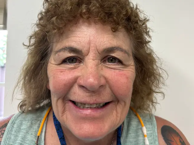 Smiling woman with curly hair, a sleeveless top, and a tattoo on her upper arm.
