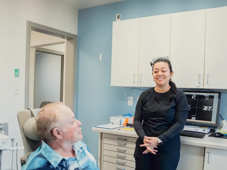 Smiling female healthcare professional talking to an elderly male patient in a medical office.