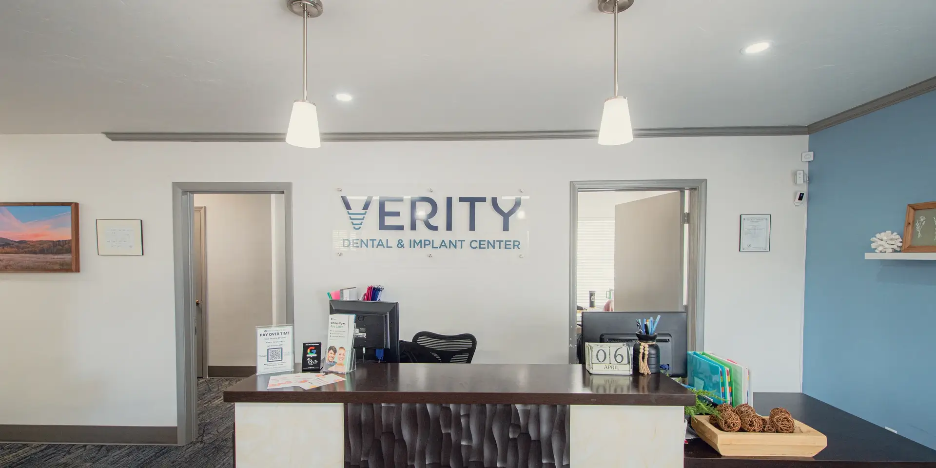 Reception desk at Verity Dental & Implant Center with computers, brochures, decorative wicker balls, and wall art.