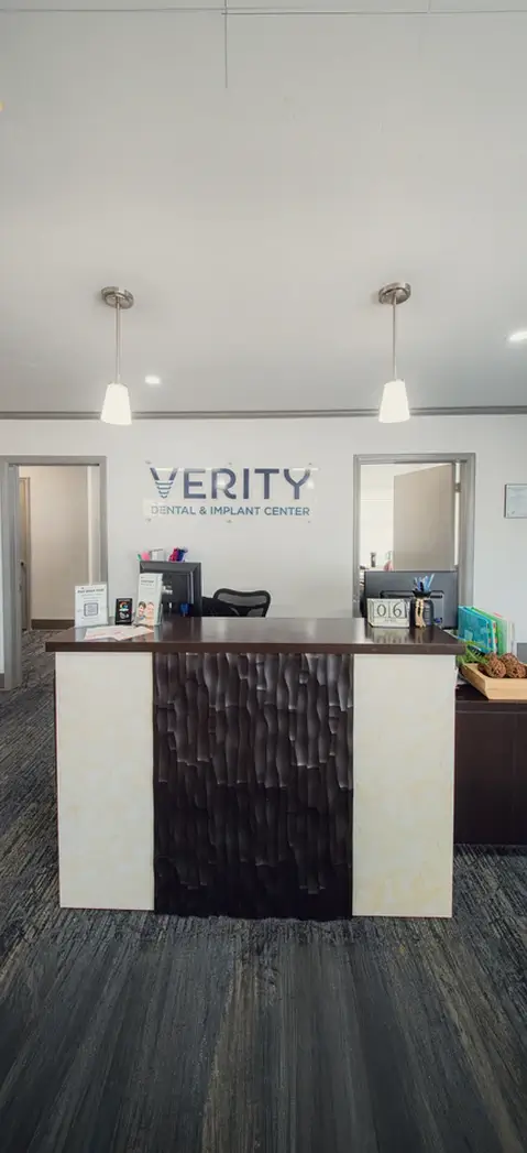 Reception desk area at Verity Dental & Implant Center with two pendant lights and open doors behind.
