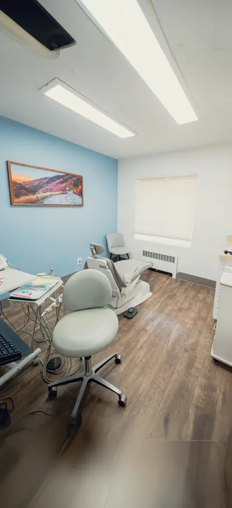 Modern dental treatment room with a dental chair, light blue accent wall, and a framed landscape photo.