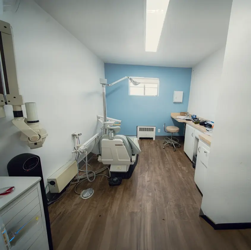Small dental examination room with dental chair, light, and surrounding cabinetry on wood-style flooring.
