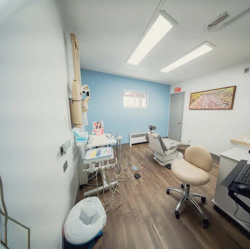 Clean, organized dental exam room with dental chair, equipment, beige stool, and a framed picture on the wall.
