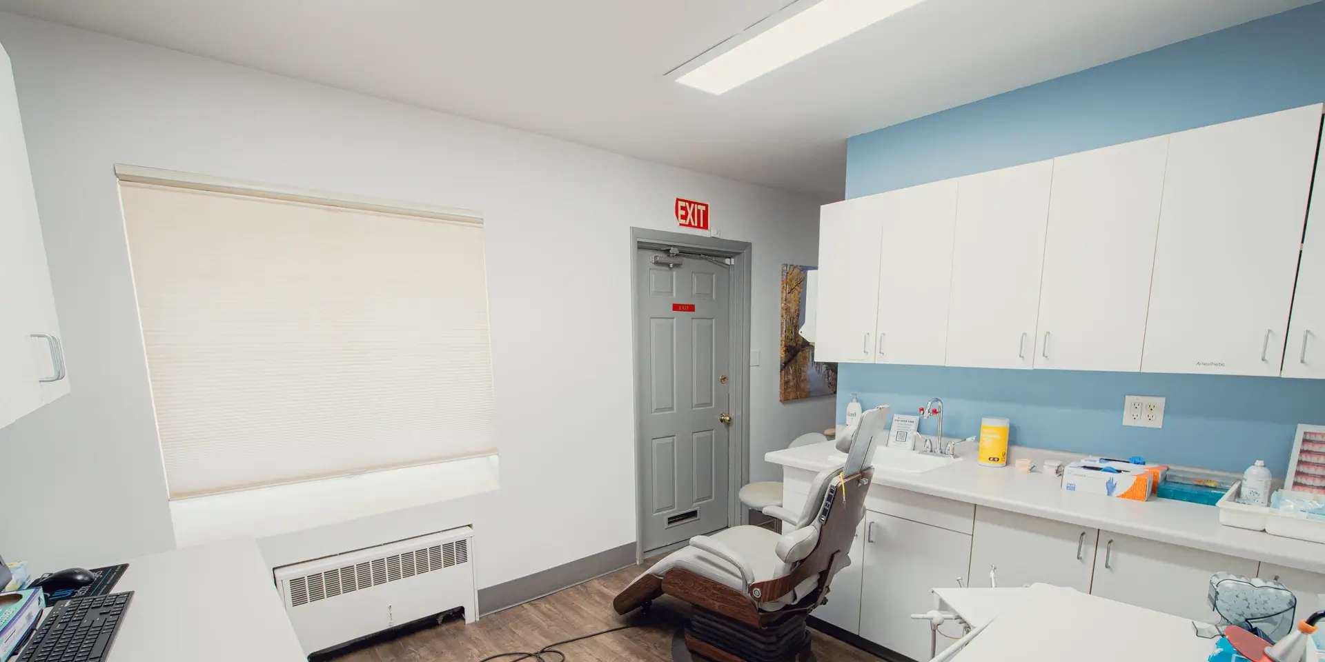 Bright dental or medical office with an examination chair, white cabinets, countertop with supplies, and an exit door.
