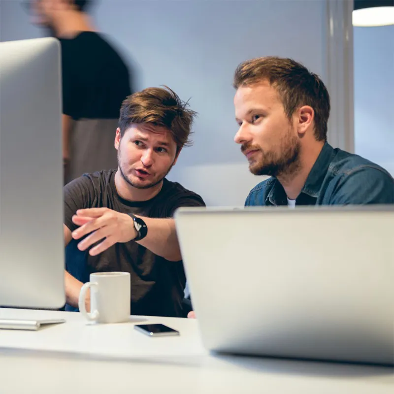Two men sitting at a table looking at a laptop.
