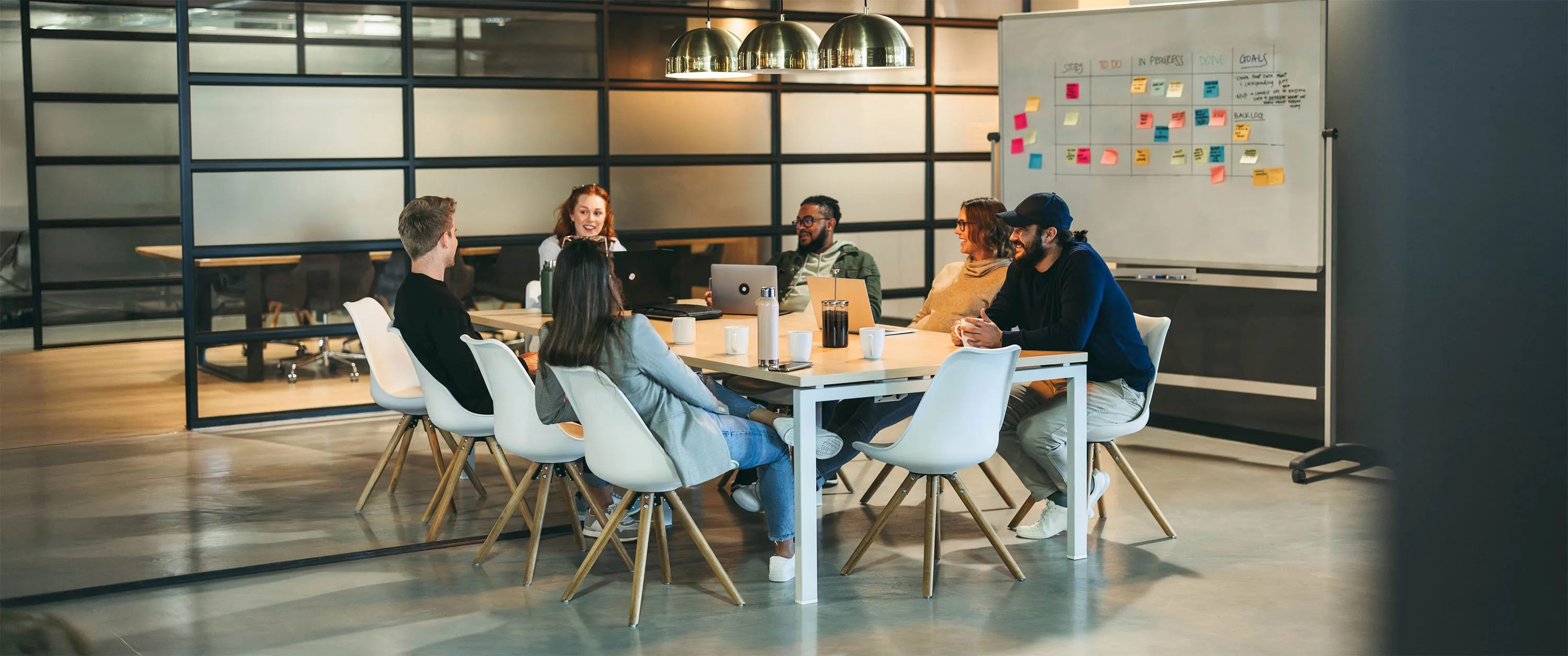 A group of people sitting around a table with whitebaord in the background