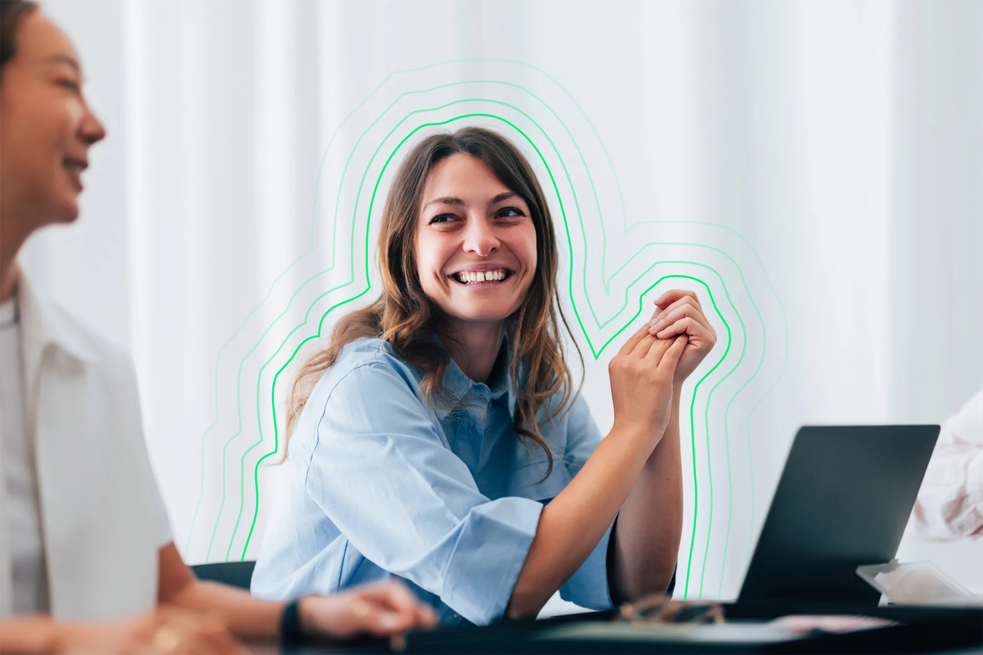A woman sitting in front of a laptop computer smiling at her colleague