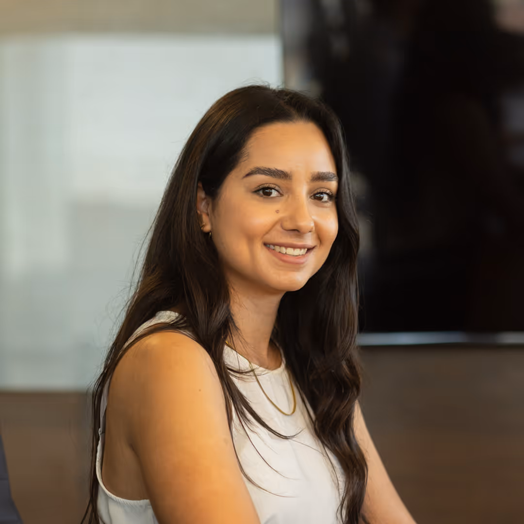 Smiling woman with long dark hair wearing a white sleeveless top and a gold necklace.