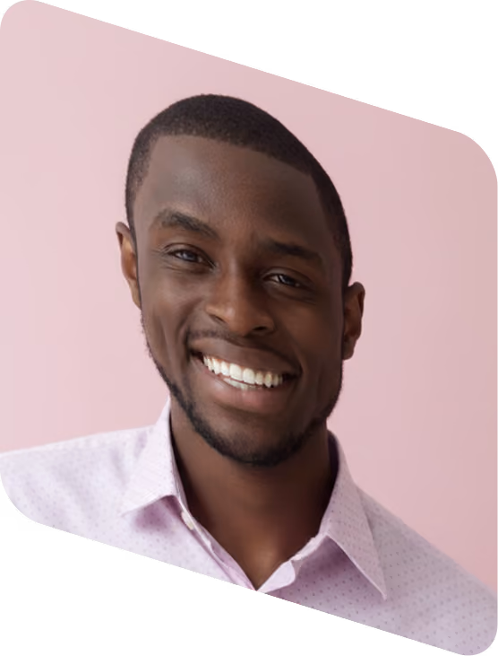 Smiling Black man wearing a light purple collared shirt against a pink background.