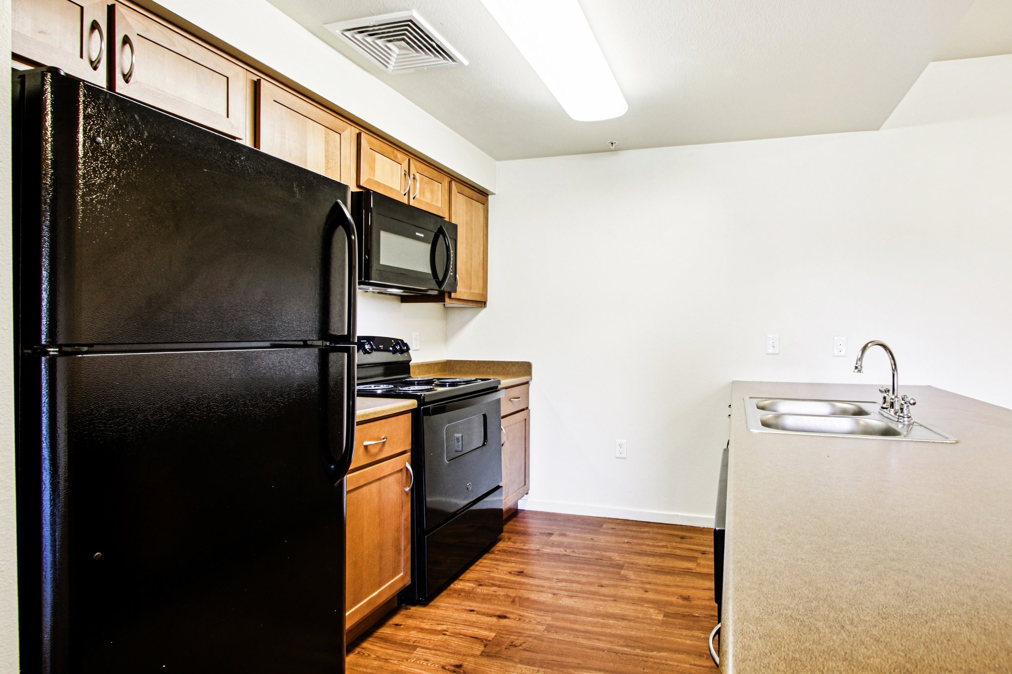Spacious kitchen with black appliances, wood cabinets, and large breakfast bar in a Copper Peak apartment home.