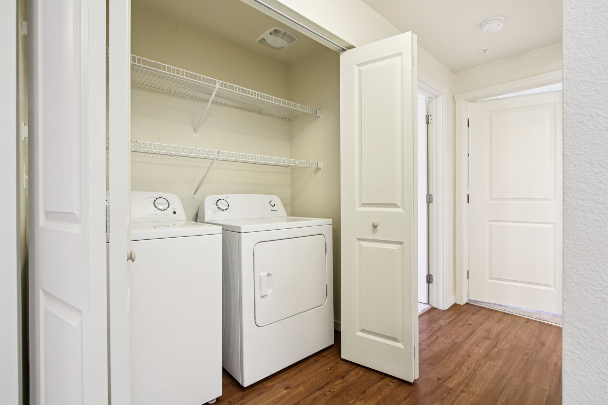 In-home washer and dryer with built-in wire shelving and additional storage at Copper Peak Apartments.